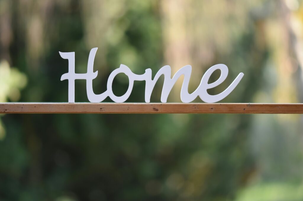 Elegant wooden 'Home' sign against a blurred green background, perfect for cozy decor themes.