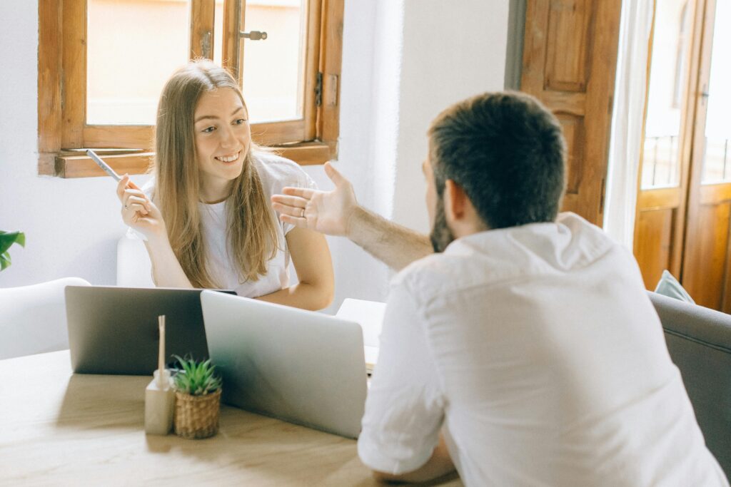 A man and woman discussing ideas while working remotely with laptops in a cozy home setting.